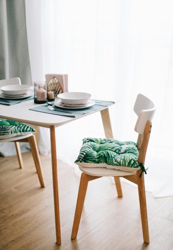 Contemporary dining room with wooden furniture and green-leaf cushions. Bright and inviting.
